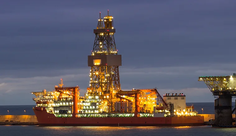 Drillship and offshore drilling rig lit up in port at dusk