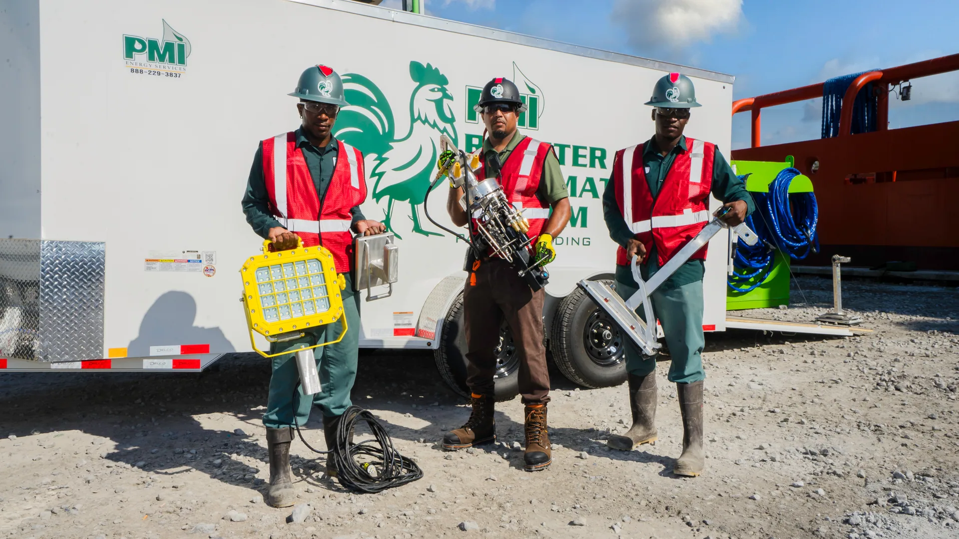 Three PMI crew members in hard hats and safety vests holding cleaning equipment in front of the RoosterEX trailer